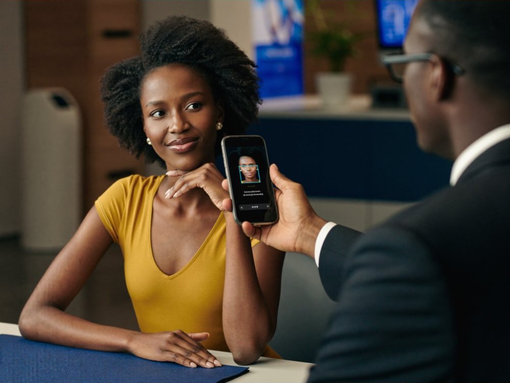 A bank customer completing face verification on a phone at a service desk